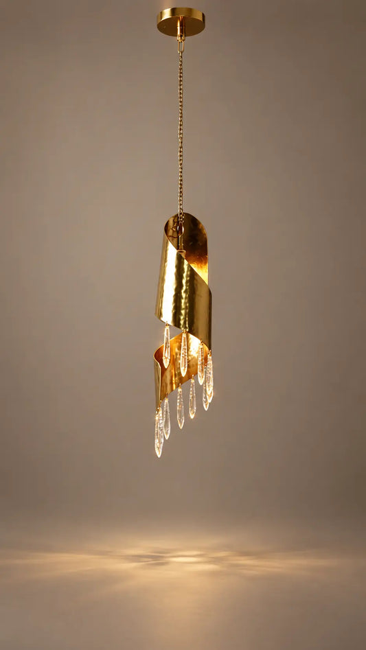 A modern gold pendant light fixture with a spiral cylindrical design and hanging clear crystal prisms, shown against a neutral gray background with warm light reflection below.